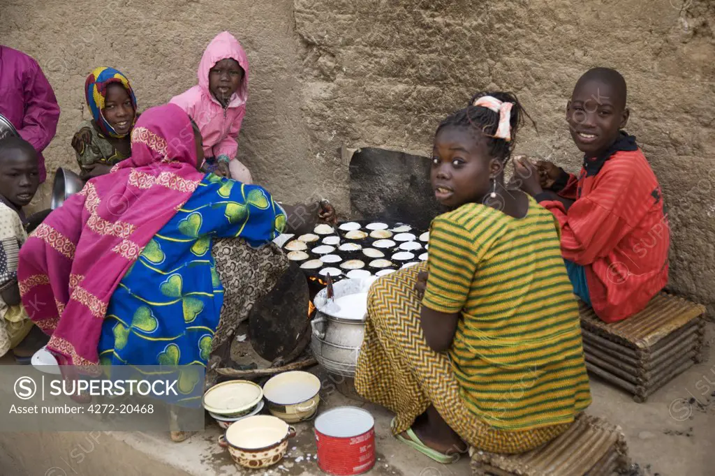 Mali, Djenne. Surrounded by her children, a woman cooks muffins on a wood stove at the side of a street leading to Djenne market. The weekly Monday market is thronged by thousands of people and is one of the most colourful in West Africa.