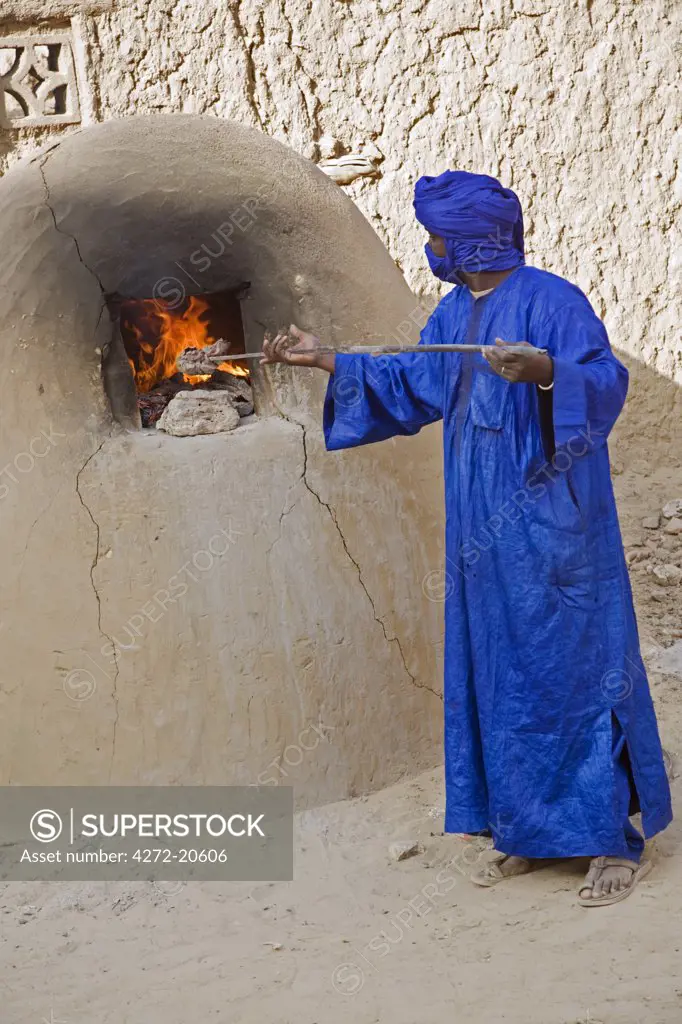 Mali, Timbuktu. A Tuareg man stokes the fire of a bread oven in Timbuktu.