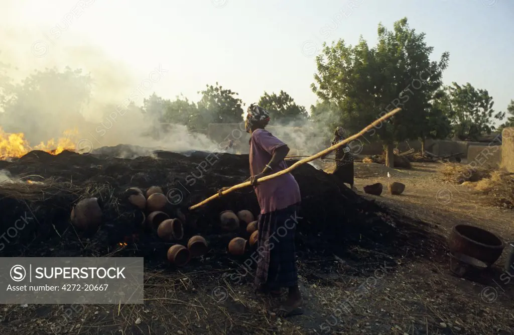 Mali, near Segou, Kalabougou. A woman rakes a fire in which pottery - for which this village is famous - is baked.