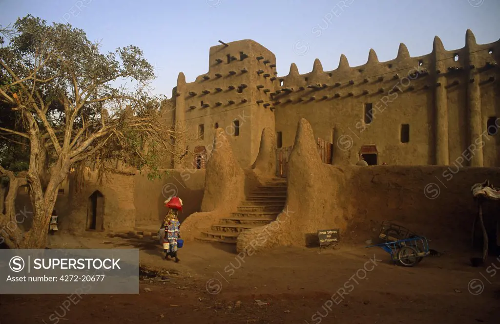 Mali, Djenne. A woman walks past the celebrated Mosque of Djenne, or Grande Mosquee, one of Africa's most striking mud brick buildings.