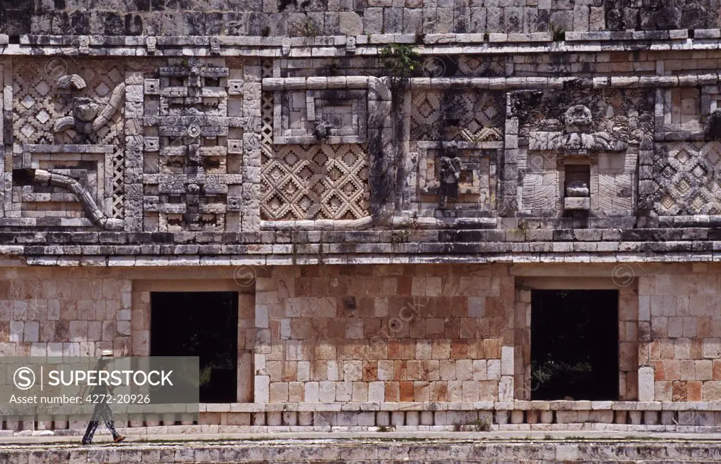 Mexico, Yucatan, Uxmal. A female tourist walks through 'The Nunnery' quadrangle at the Mayan site of Uxmal. This is one of the best preserved Mayan sites displaying the 'Puuc' style of architecture, named after the Puuc Hills nearby.