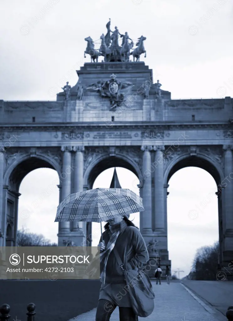Belgium, Brussels; A girl walking with an umbrella in front of the Arc du Triomphe