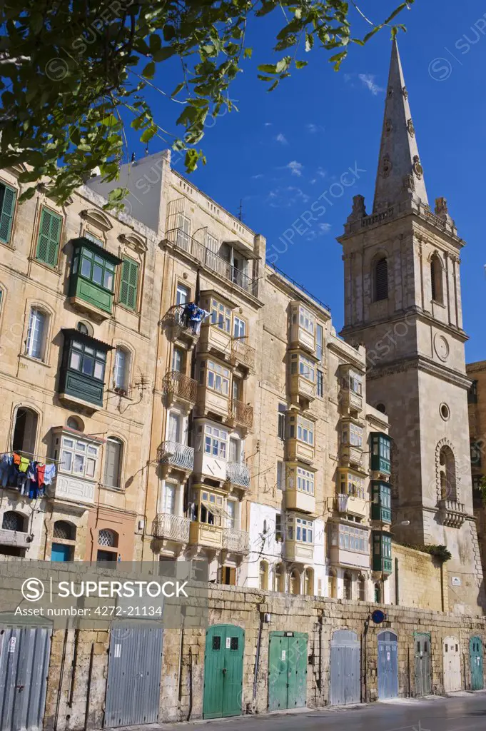 Malta, Valletta. A church spire rises up above closely packed apartments and garages built into the old walls of the city.