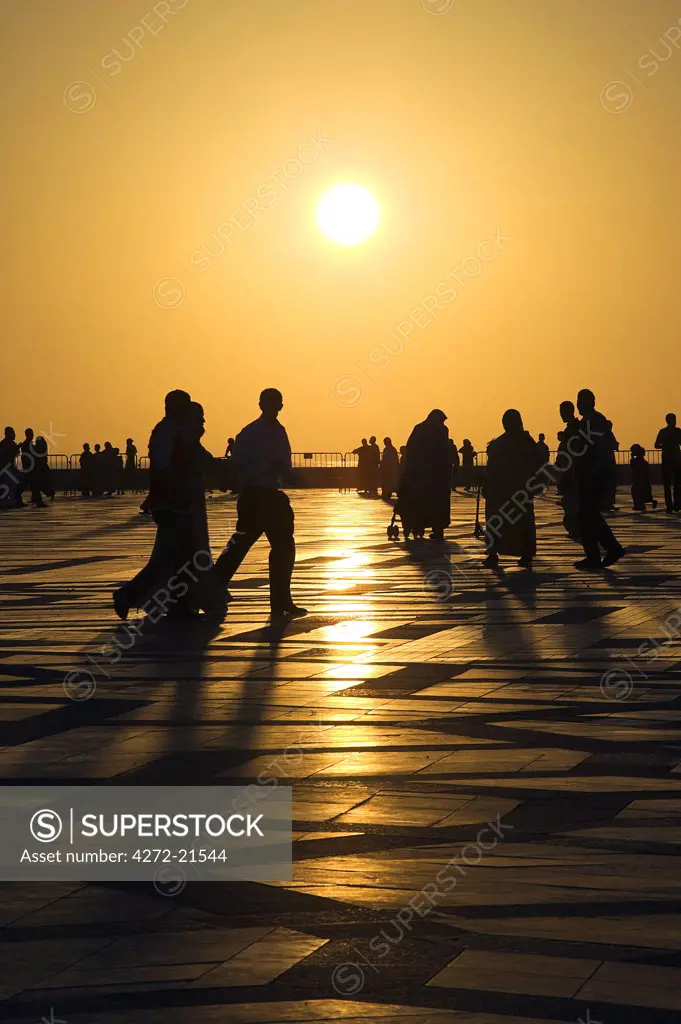Families and friends enjoy an evening stroll, or paseo, under the setting sun in the courtyard of the Hassan II Mosque in Cassablanca.