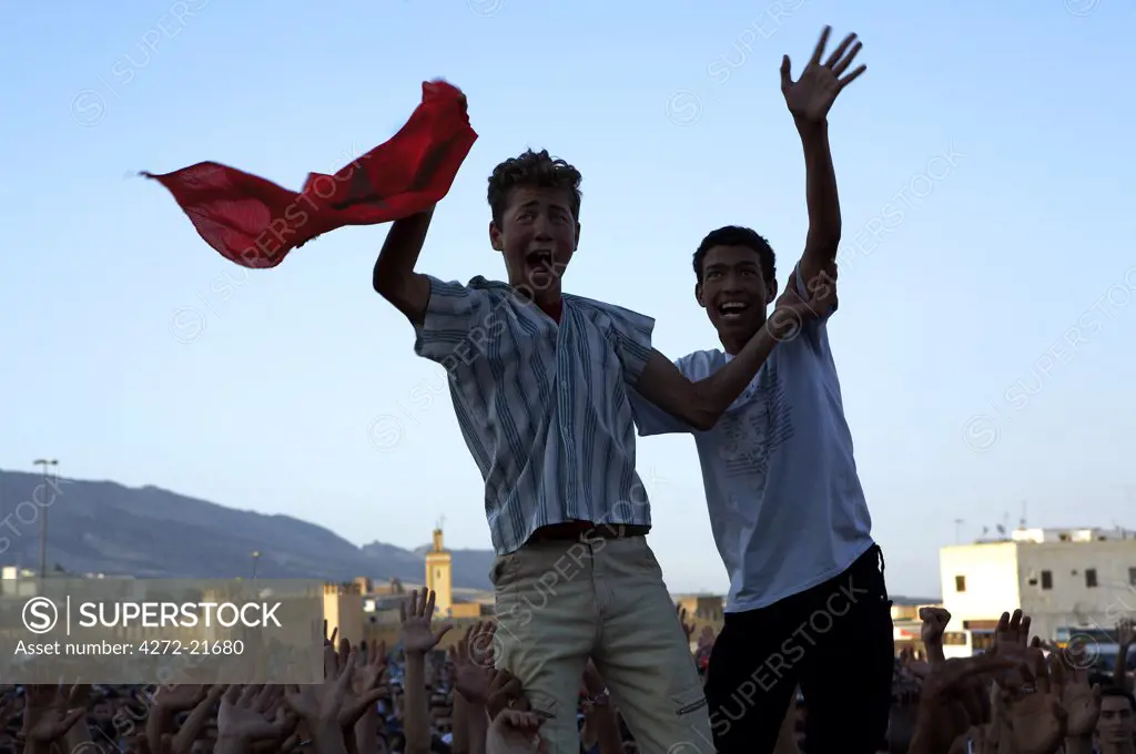 Morocco, Fes.  Two proud Moroccan boys wave their national flag above the crowds at a concert in the Place Boujloud, during the Fes Festival of World Sacred Music.
