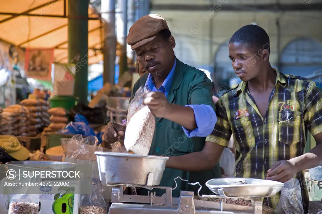 Mozambique, Maputo. A stall holder weighs his produce with the help of his assistant in the Central Market in downtown Maputo. The Central Market, commonly known as Mercardo Central, is on Avenida 25 de Abril in downtown Maputo. The market is a good place to buy a variety of fresh and frozen fish aswell as vegetables, fruit, carvings, and baskets.
