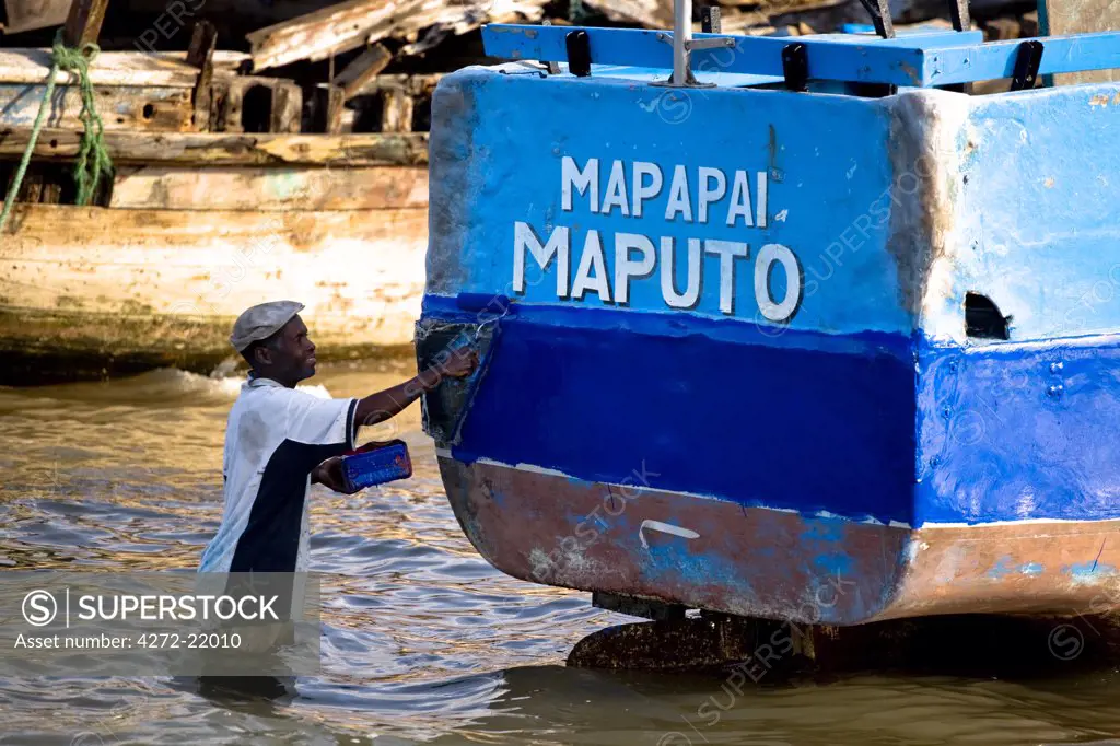 Mozambique, Maputo. A man gives his boat a fresh coat of paint in the village of Catembe close to Maputo. Maputo is the capital of Mozambique. It is a bustling, attractive port city with a population of at least 1.5 million.  Maputo is a very agreeable city which is considerably safe and more attractive when compared to other African capitals.