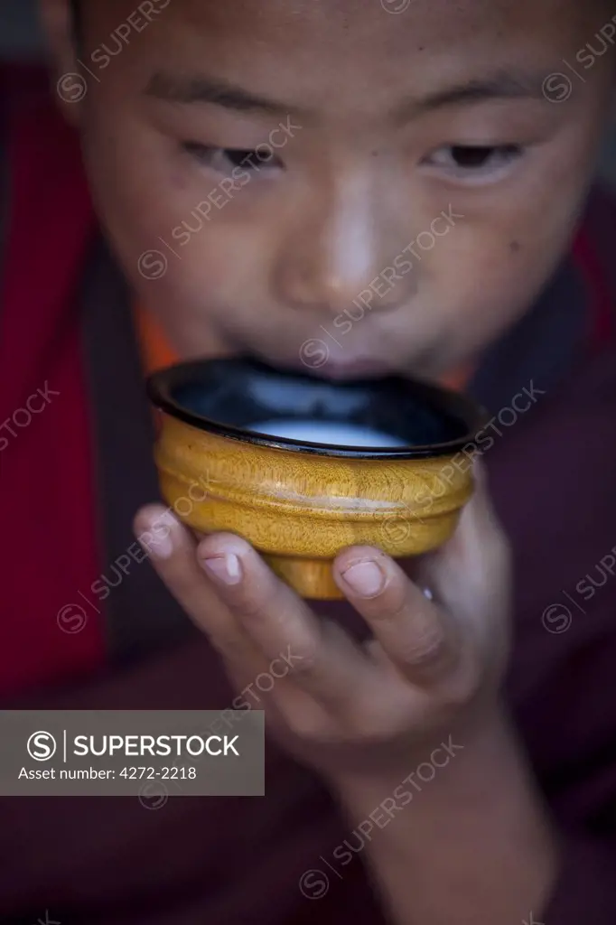 A young monk drinking milk from a wooden bowl in Bhutan