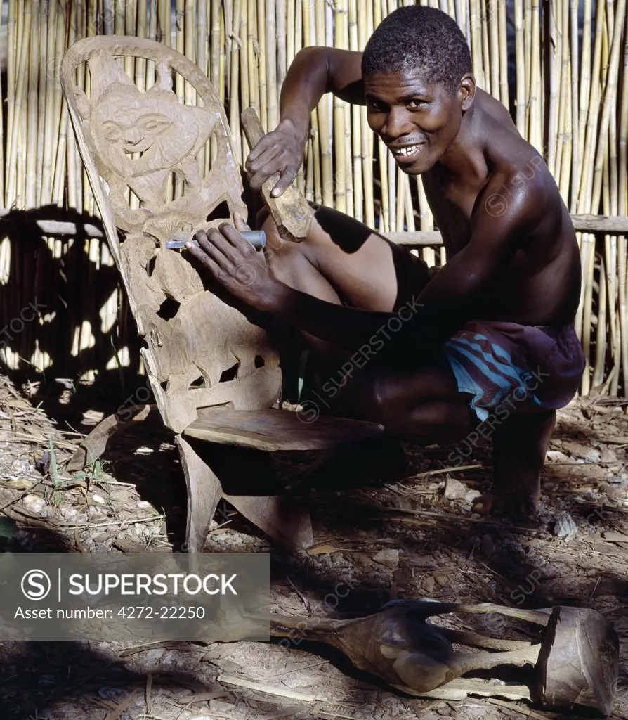 A wood carver puts the finishing touches to a Chief's chair. These two-piece, three-legged stools with high, decorated backs are beautifully made from hard wood and have become popular with tourists.