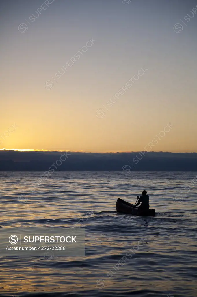 Malawi, Monkey Bay. A lone fisherman paddles out on Lake Malawi as dawn breaks.