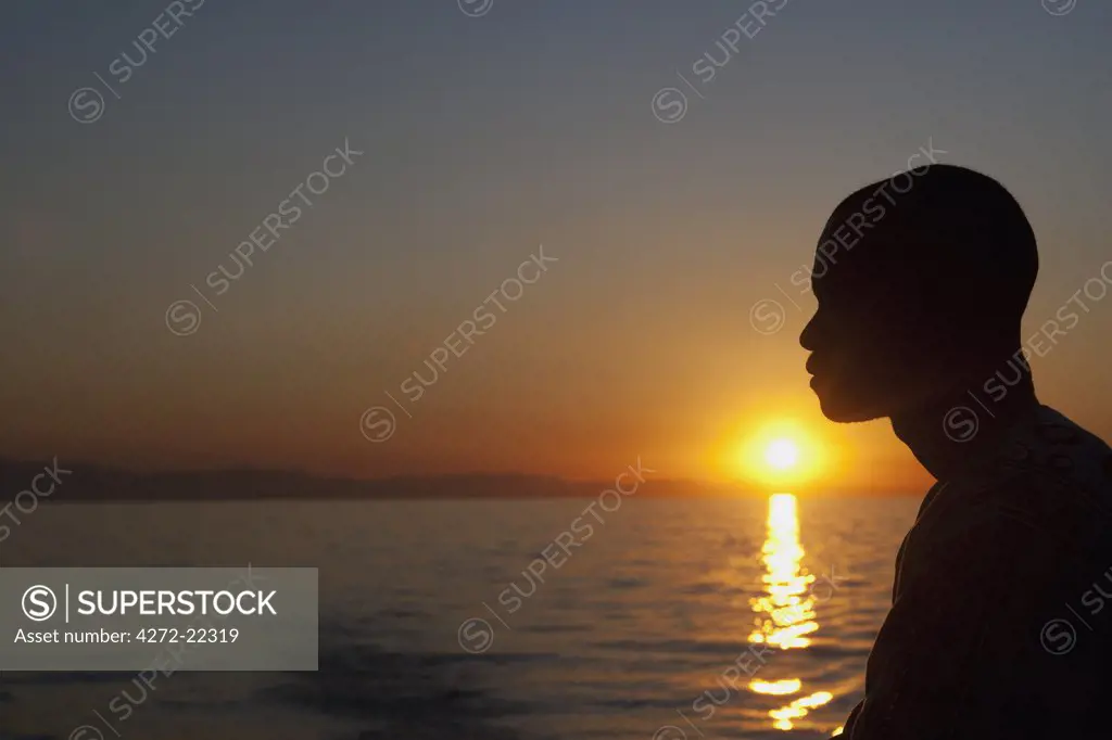 Malawi, Lake Malawi; sunset over the lake a local boatmen outlined by the setting sun.