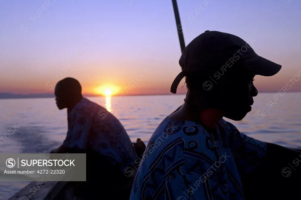 Malawi, Lake Malawi; sunset over the lake with the head of local boatmen outlined by the setting sun.