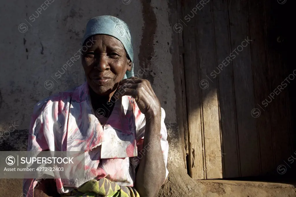 Malawi, Lilongwe, Ntchisi Forest Reserve. An old woman sits by the entrance to her hut in a mountain village.