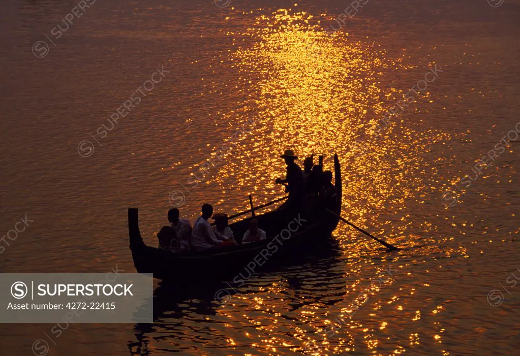 A man rows a local wooden boat across the Irrawaddy River at sunset