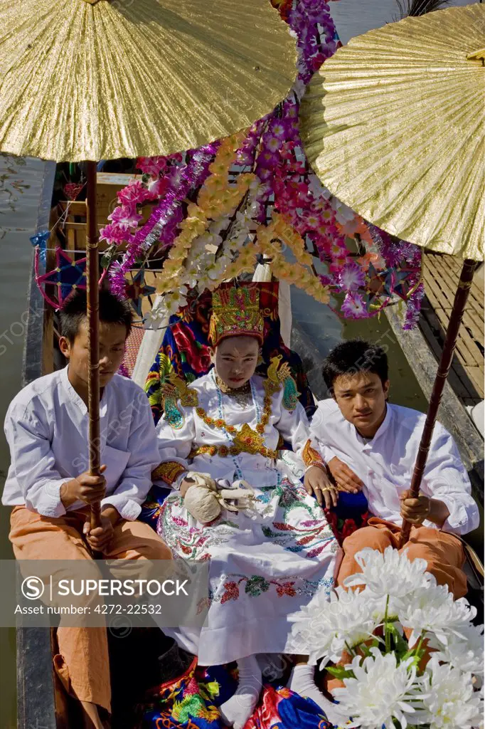 Myanmar, Burma, Lake Inle. A young novitiate shaded with golden umbrellas during a ceremony in which the boy is inducted as a novice Buddhist monk.
