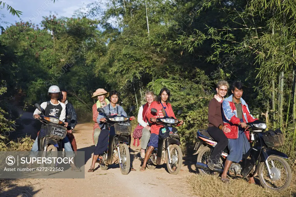 Myanmar, Burma, Lake Inle. A group of tourists ride pillion on rough tracks to visit the Pa-O village of Kya-Toon in the hills beyond Indein.