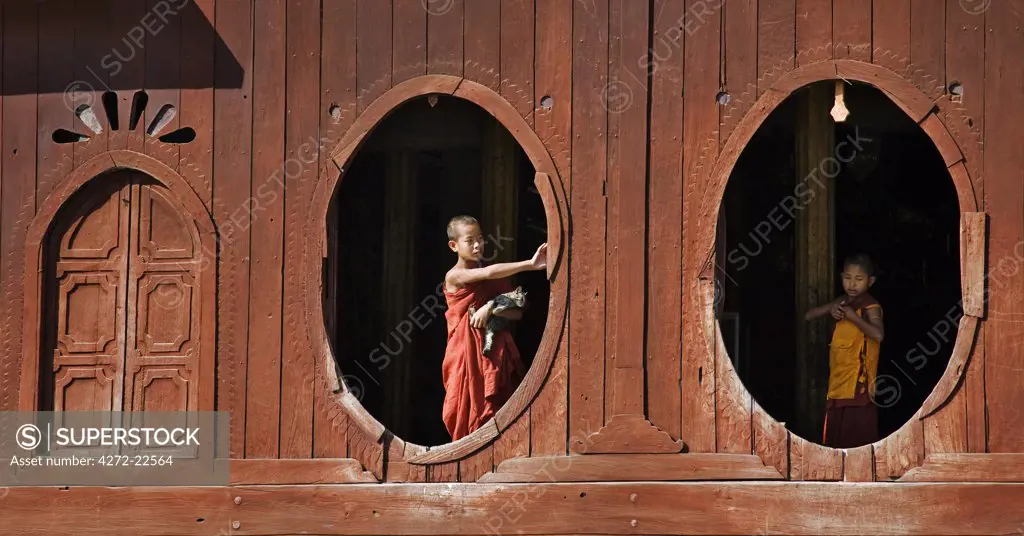 Myanmar. Burma. Nyaung-shwe. Young novice monks at the oval windows of the attractive wooden thein or ordination hall of the mid-19th century Shwe Yaunghwe monastery.