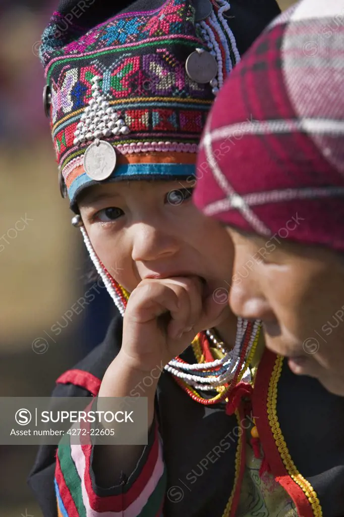 Myanmar, Burma, Kengtung. A young Akha boy wearing a colourful embroidered hat while carried by his mother.