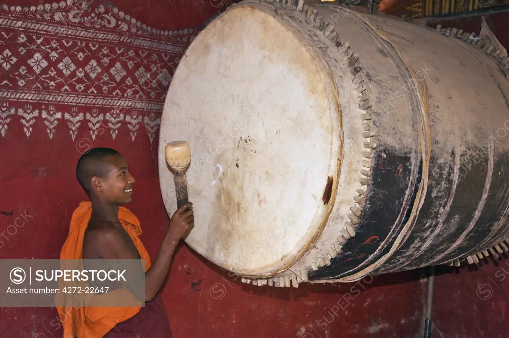 Myanmar, Burma, Wan-seeing.  A novice monk beats the huge drum inside the beautiful 15th or 16th century Wan-seeing monastery.