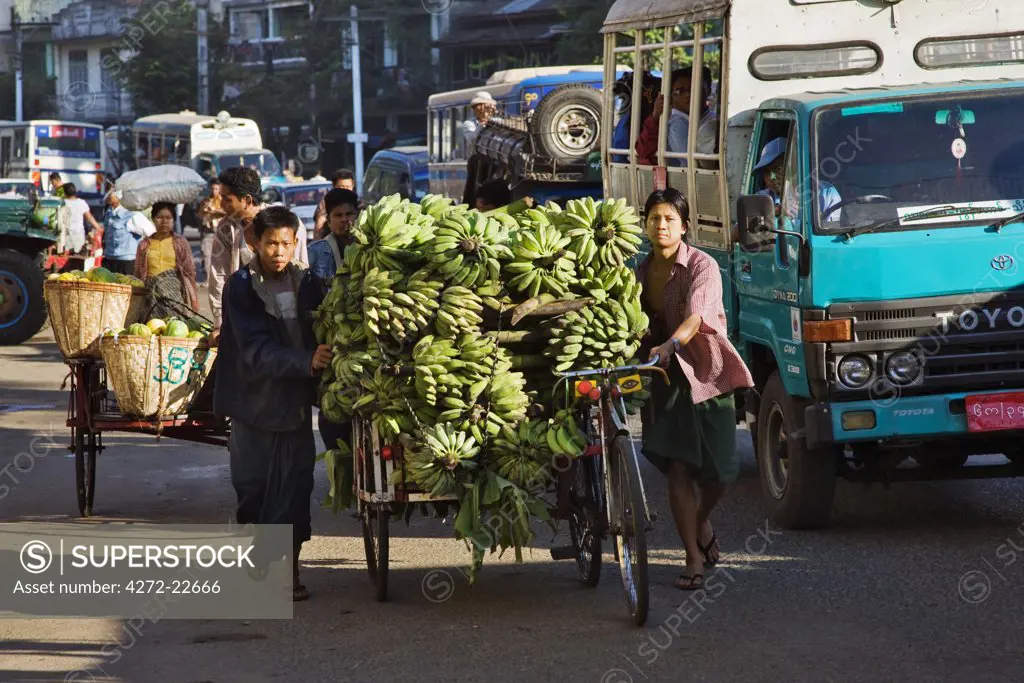 Myanmar, Burma, Yangon. A busy street scene in Yangon with trishaws laden with fruit heading for market.
