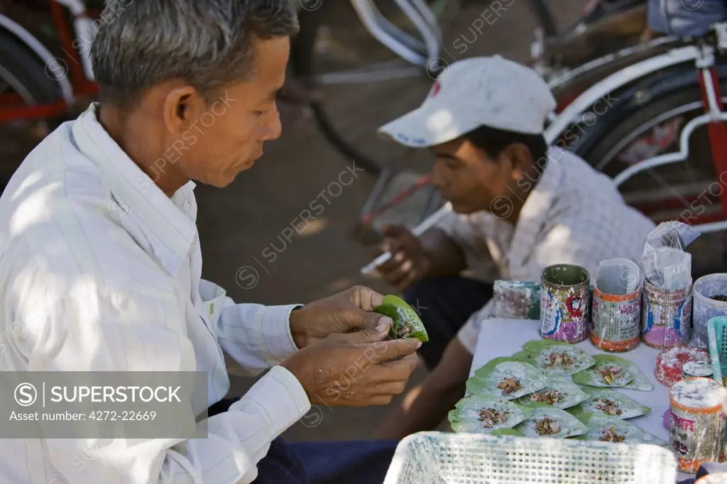 Myanmar, Burma, Yangon. The owner of a small street stall prepares beetle nut wrapped in lime-coated betel leaves.  When chewed, it acts as a mild stimulant staining the mouth deep red.