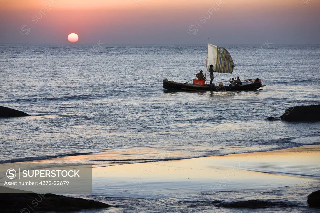 Myanmar, Burma, Rakhine State. The crew of a fishing boat hurries home to Sittwe as the sun sets over the Bay of Bengal.