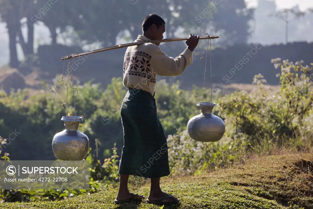 Myanmar, Burma, Mrauk U. A Rakhine man carries water in aluminium pots near Mrauk U.