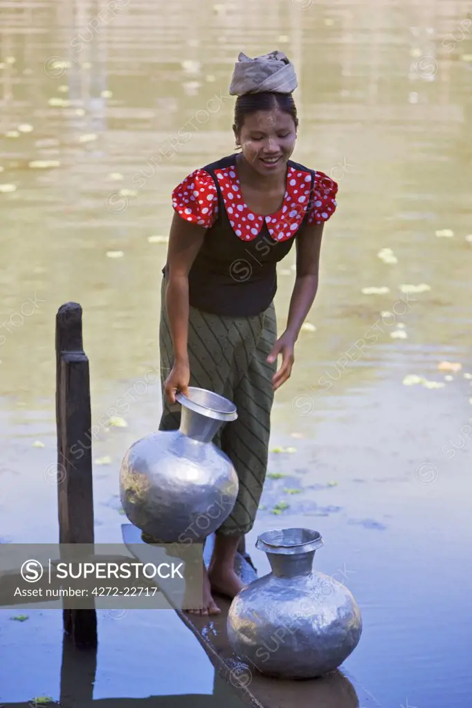 Myanmar, Burma, Mrauk U. A young Rakhine woman draws water in aluminium pots from a rainwater pond near her village.