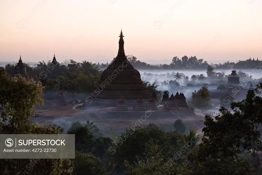 Myanmar, Burma, Mrauk U. Smoke swirls around the historic bell-shaped temples of Mrauk U at dusk. They were built in the Rakhine style between the 15th and 17th centuries.