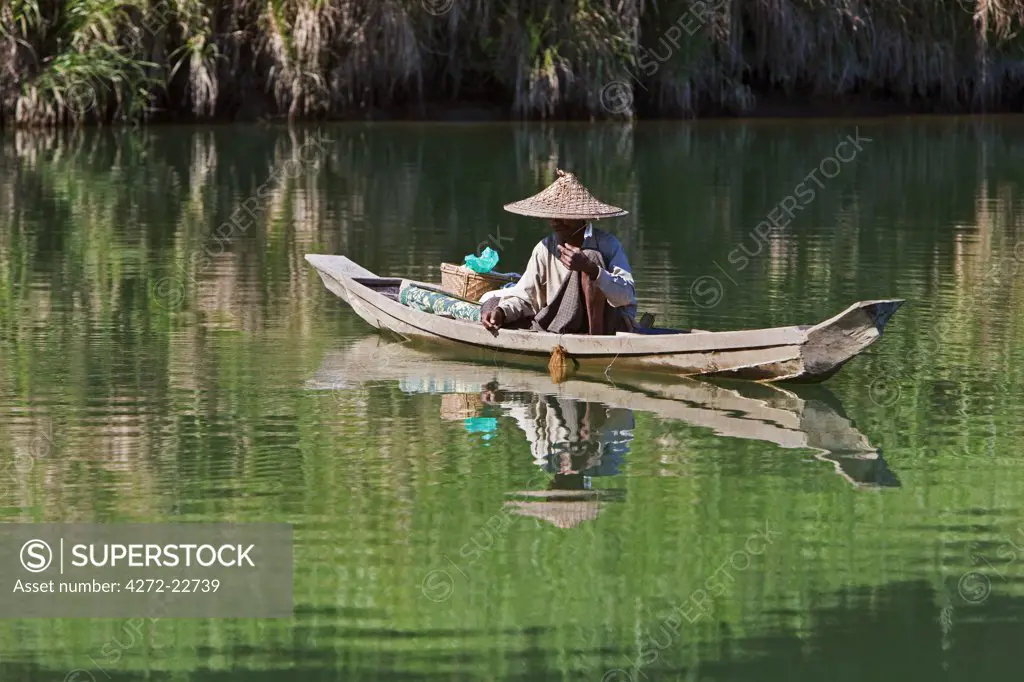 Myanmar, Burma, Lay Mro River. A Rakhine man fishes from a small wooden boat in the still waters of the Lay Myo River.