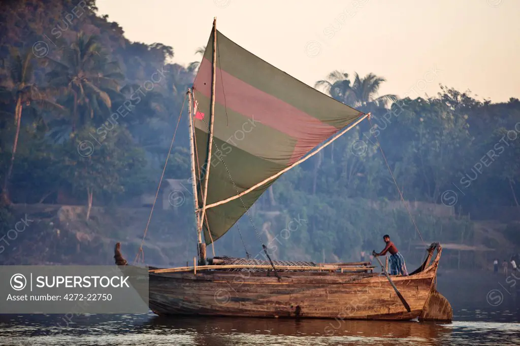 A large wooden boat of Rakhine design sails up the Lay Myo River in fading evening light.