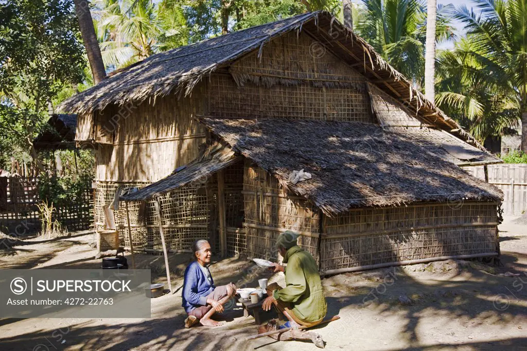 Myanmar, Burma, Rakhine State, Gyi Dawma. A bamboo house at Gyi Dawma village with the owners, an old couple, taking their morning meal outside.
