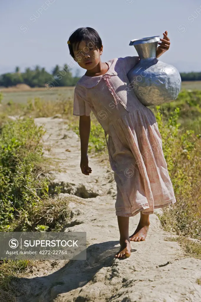 Myanmar, Burma, Rakhine State, Laung Shein. A young girl from Laung Shein village collects water from a nearby dam. Her face is decorated with Thanakha, a local sun cream and skin lotion.