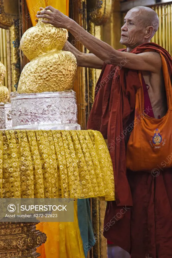 Myanmar, Burma, Inle Lake. A monk applies gold leaf to one of five buddha images, now transformed into a blob by the sheer volume of gold leaf applied over the years, Phaung Daw Oo Paya.