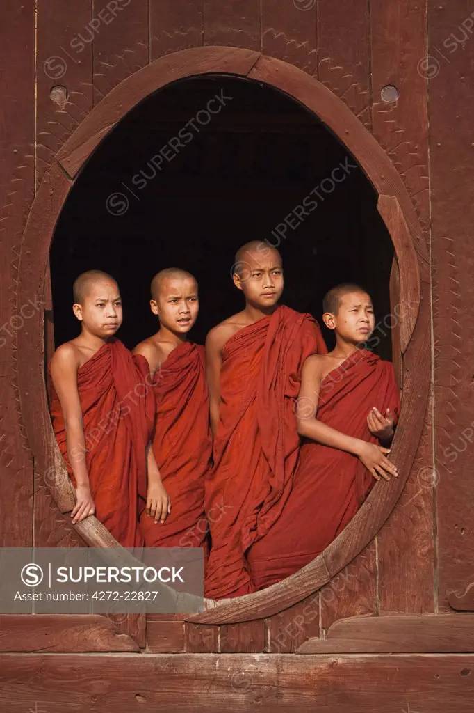 Myanmar, Burma, Nyaungshwe. Young novice monks standing at a wooden oval window, Shwe Yaunghwe Kyaung monastery.