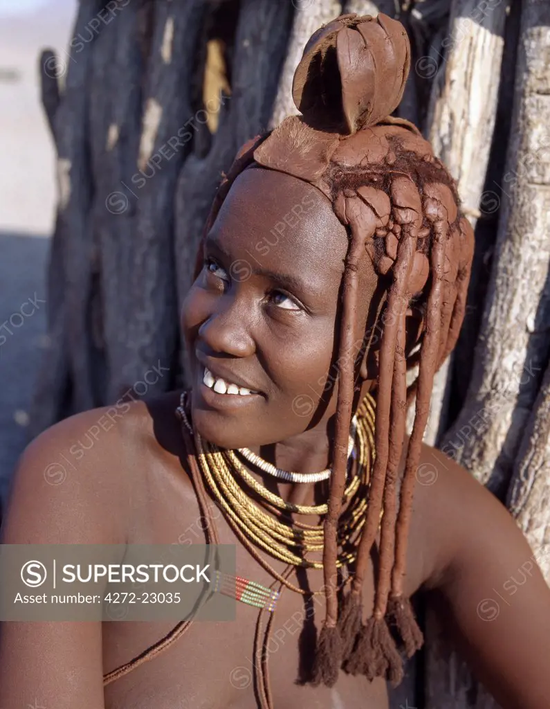 A Himba woman in traditional attire. Her body gleams from a mixture of red ochre, butterfat and herbs.  Her long hair is styled in the traditional Himba way and is crowned with a headdress made of lambskin, which is called erembe.