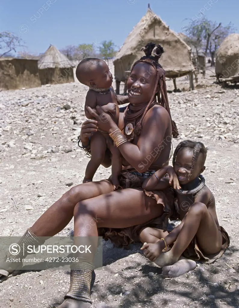 A Himba mother and children in traditional attire. Their bodies gleam from a mixture of red ochre, butterfat and herbs.  The womans long hair is styled in the traditional Himba way and is crowned with a headdress made of lambskin, which is called erembe. The Himba are Herero speaking Bantu nomads who live in the harsh, dry but starkly beautiful landscape of remote northwest Namibia.