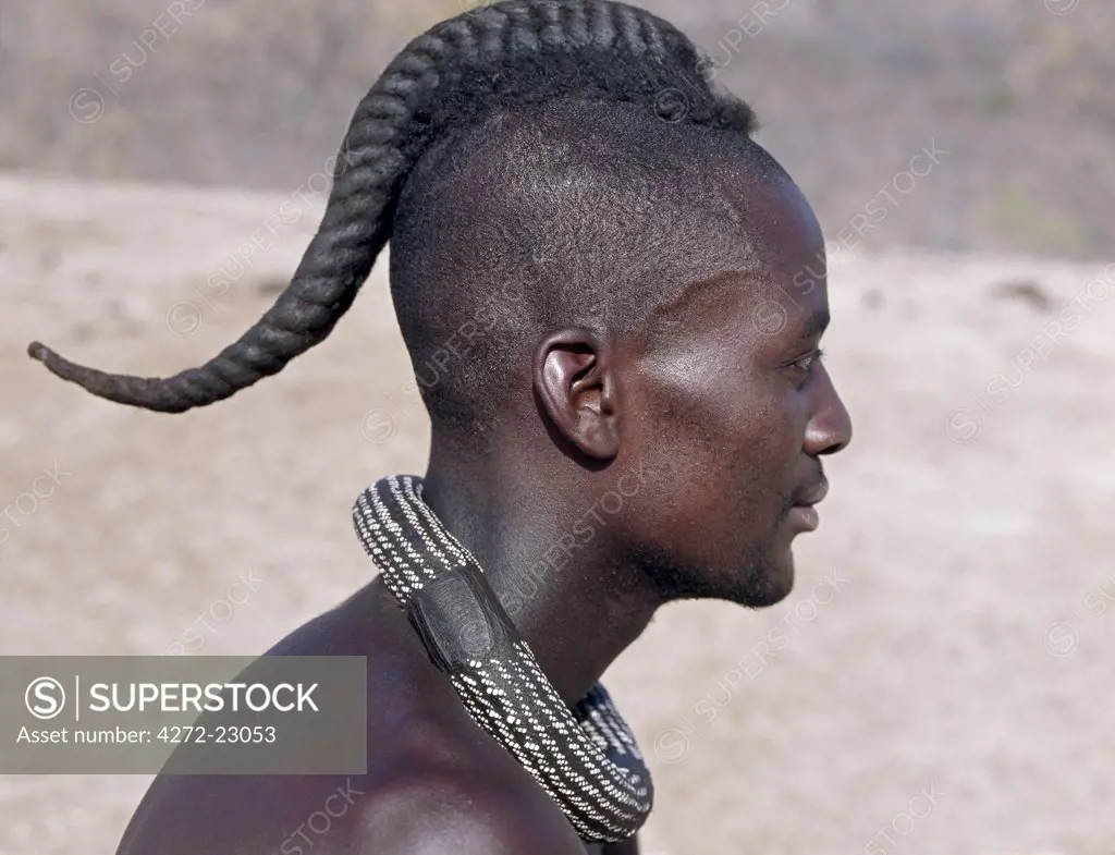A Himba youth has his hair styled in a long plait, known as ondatu. Once married, he will split the ondatu into two plaits and keep them covered.  The Himba are Herero speaking Bantu nomads who live in the harsh, dry but starkly beautiful landscape of remote northwest Namibia.