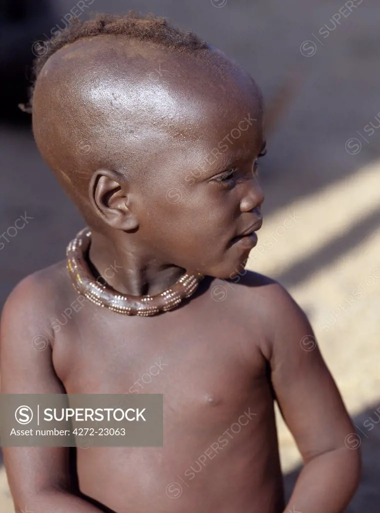 A small girl, her body smeared with a mixture of red ochre, butterfat and herbs, wears a round white beaded necklace, called ombwari, a tradition of all Himba people. The Himba are Herero speaking Bantu nomads who live in the harsh, dry but starkly beautiful landscape of remote northwest Namibia.