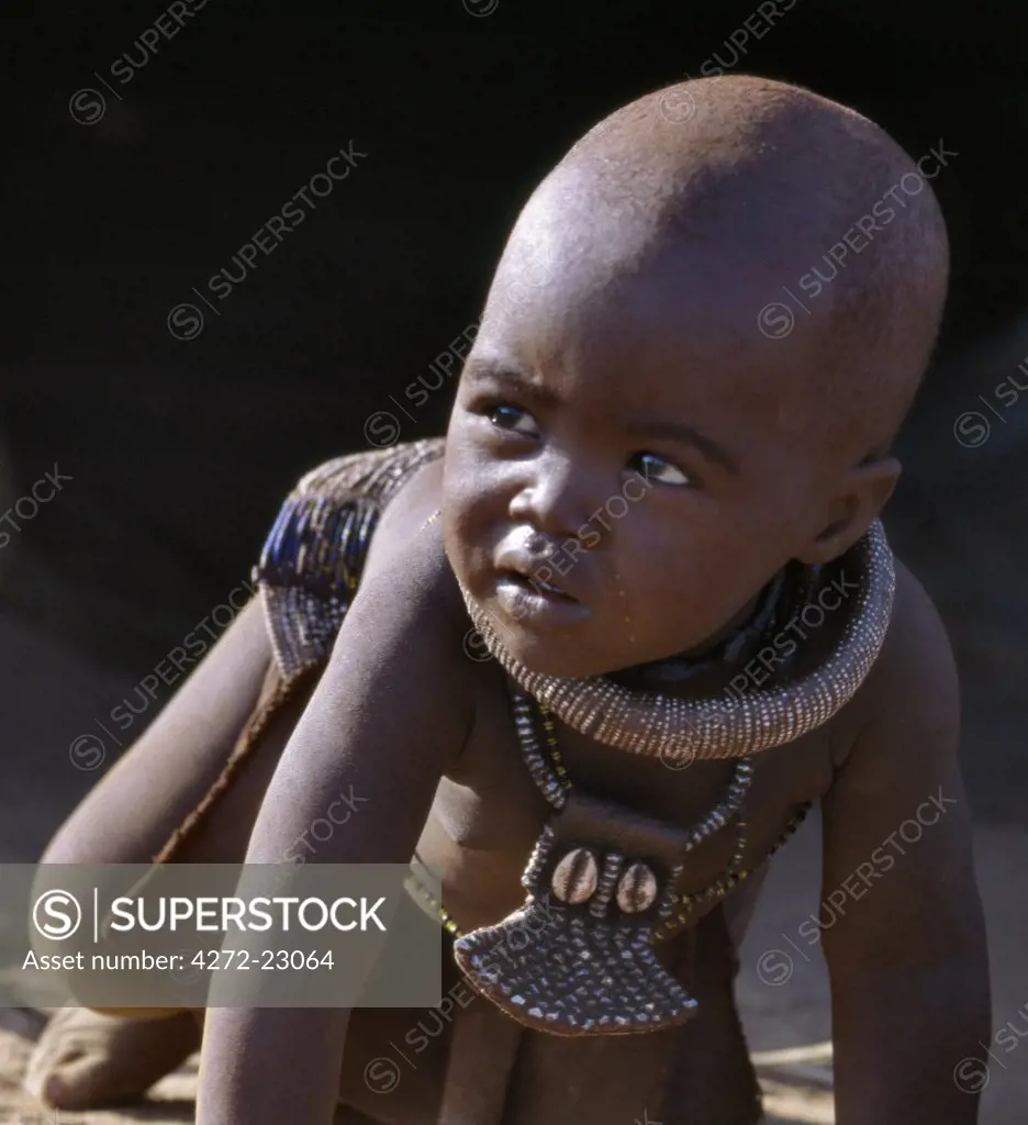 A small boy, his body smeared with a mixture of red ochre, butterfat and herbs, wears a round white beaded necklace, called ombwari, a tradition of all Himba people. The Himba are Herero speaking Bantu nomads who live in the harsh, dry but starkly beautiful landscape of remote northwest Namibia.