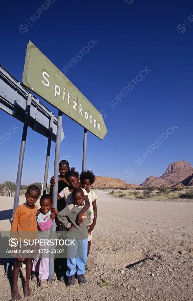 Local children by Spitzkoppe sign with massif in background.