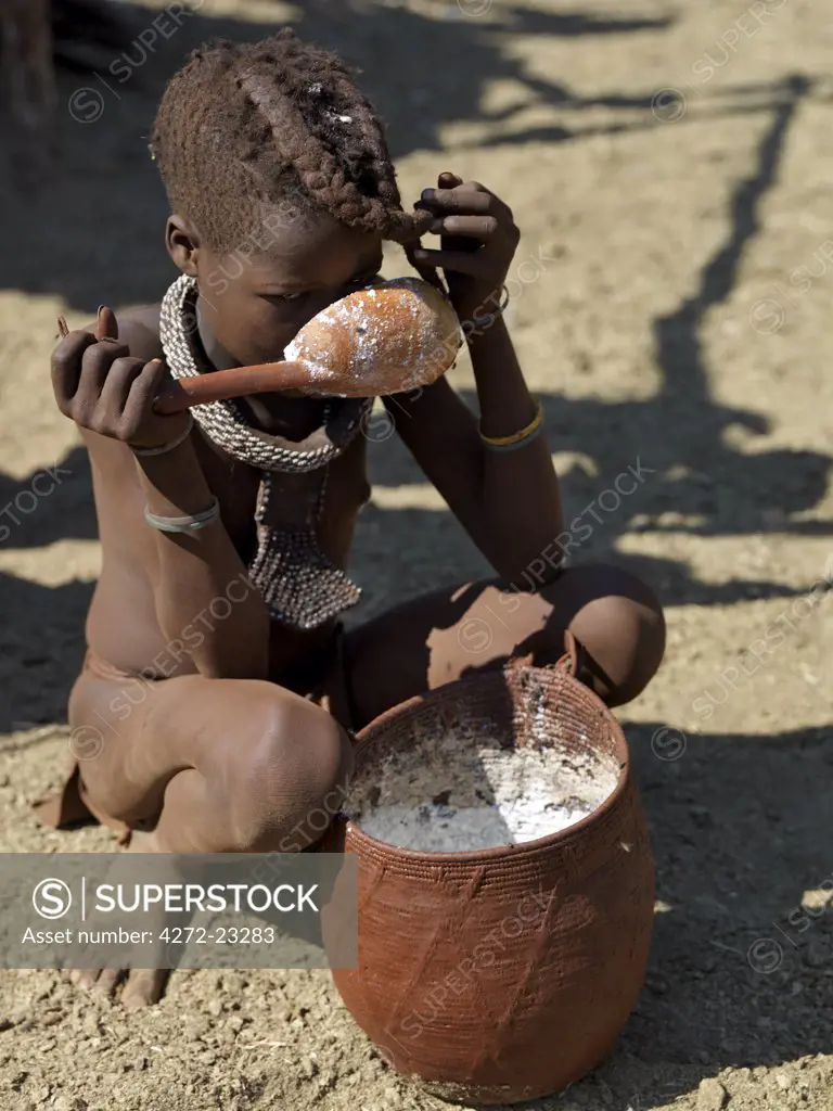 A Himba girl drinks milk with a wooden spoon from a beautifully made woven container made from local grasses, which is plastered with animal fat and ochre on the outside to prevent it leaking.The Himba are Herero speaking Bantu nomads who live in the harsh, dry but starkly beautiful landscape of remote northwest Namibia.