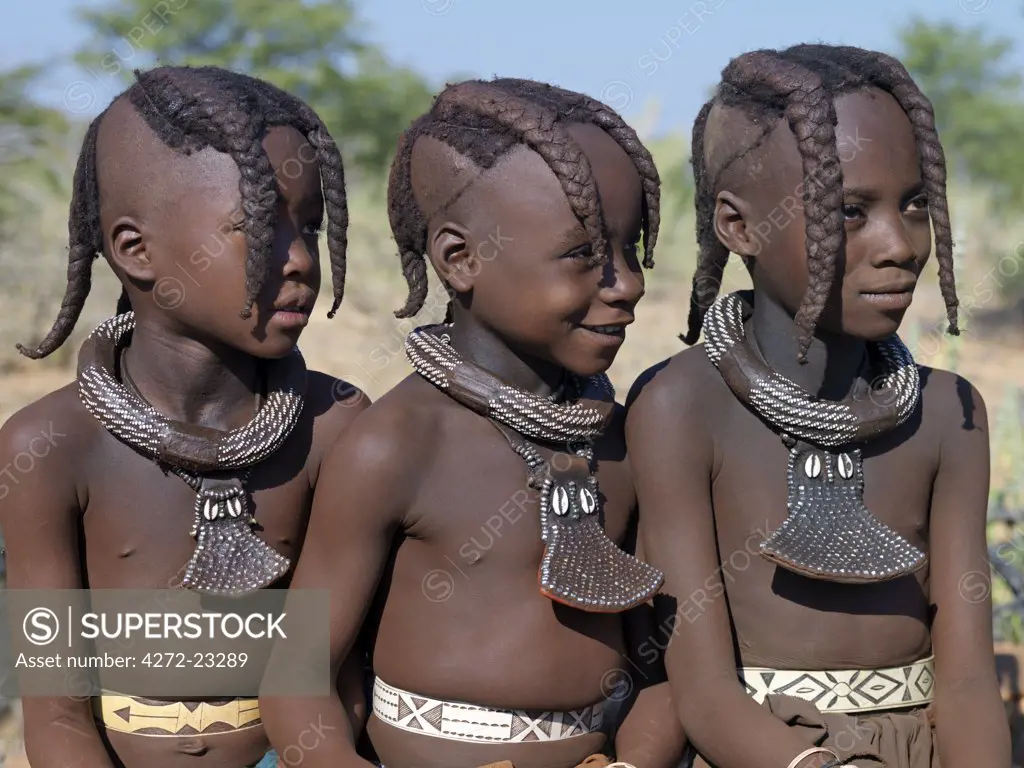 Three young girls, their bodies lightly smeared with a mixture of red ochre, butterfat and herbs, wears a round white beaded necklace, called ombwari, a tradition of all Himba people. The Himba are Herero speaking Bantu nomads who live in the harsh, dry but starkly beautiful landscape of remote northwest Namibia.