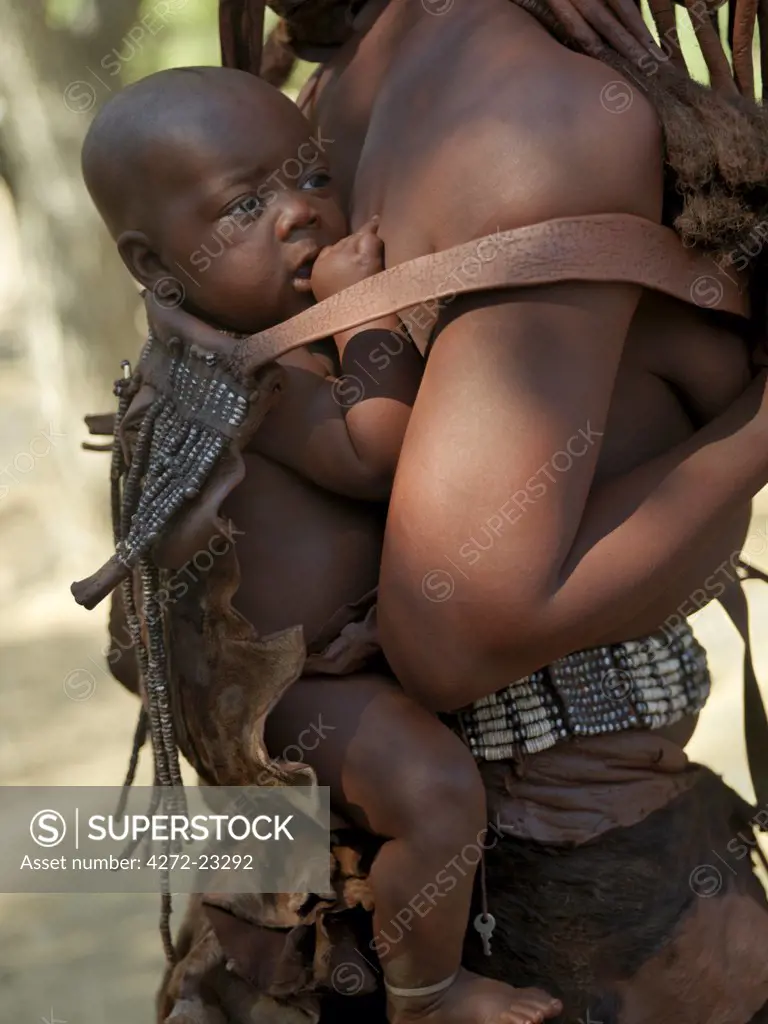 A child is carried on his mothers back in a beautifully decorated leather carrier. The Himba are Herero speaking Bantu nomads who live in the harsh, dry but starkly beautiful landscape of remote northwest Namibia.