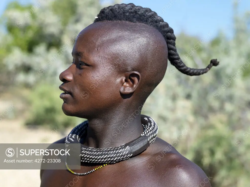 A Himba youth with his hair styled in a long plait, known as ondatu. Once married, he will split the ondatu into two plaits and keep them covered. His heavy white-beaded necklace, ombwari, will have been made for him by his mother. They are worn by both men and women. The Himba are Herero-speaking Bantu nomads who live in the harsh, dry but starkly beautiful landscape of remote northwest Namibia.