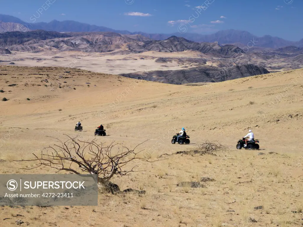 Tourists set out on quad bikes to explore the magnificent desert scenery of Hartmann's Valley, a place of outstanding natural beauty on the border of Namibia and Angola in remote northwest Namibia. The mountains in the distance are in Angola.
