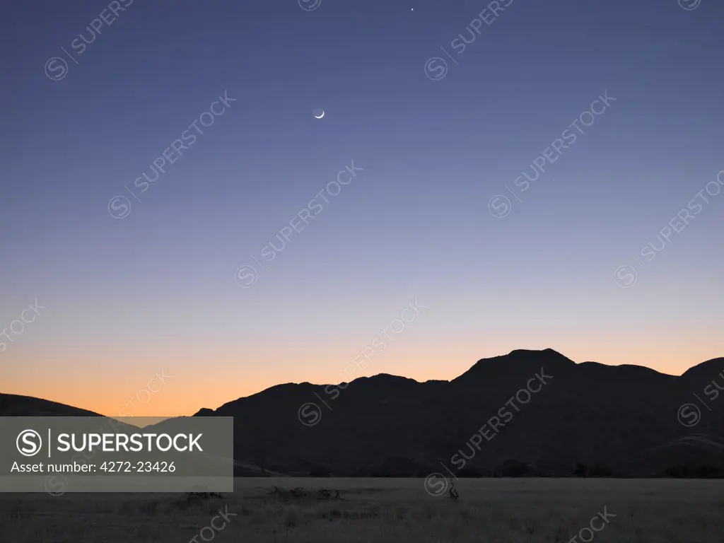 At daybreak over a range of mountains bordering the Hoanib River, the moon and morning star are clearly visible.