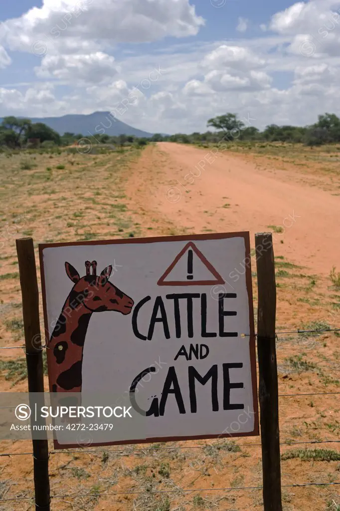 Namibia, Erongo Region. Where a dirt track bisects a bush farm, a sign on the road warns of the danger of speeding to cattle and game animals.