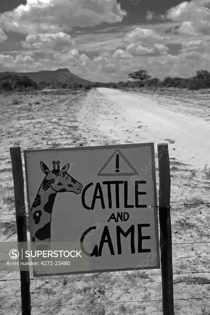 Africa, Namibia, Erongo Region.  Where a dirt bisects a bush farm a sign on the road warns of the danger of speeding to cattle and game animals.