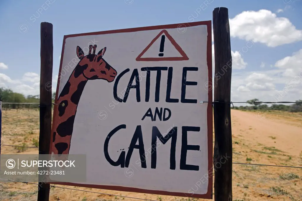 Africa, Namibia, Erongo Region. Where a dirt track bisects a bush farm, a sign on the road warns of the danger of speeding to cattle and game animals.